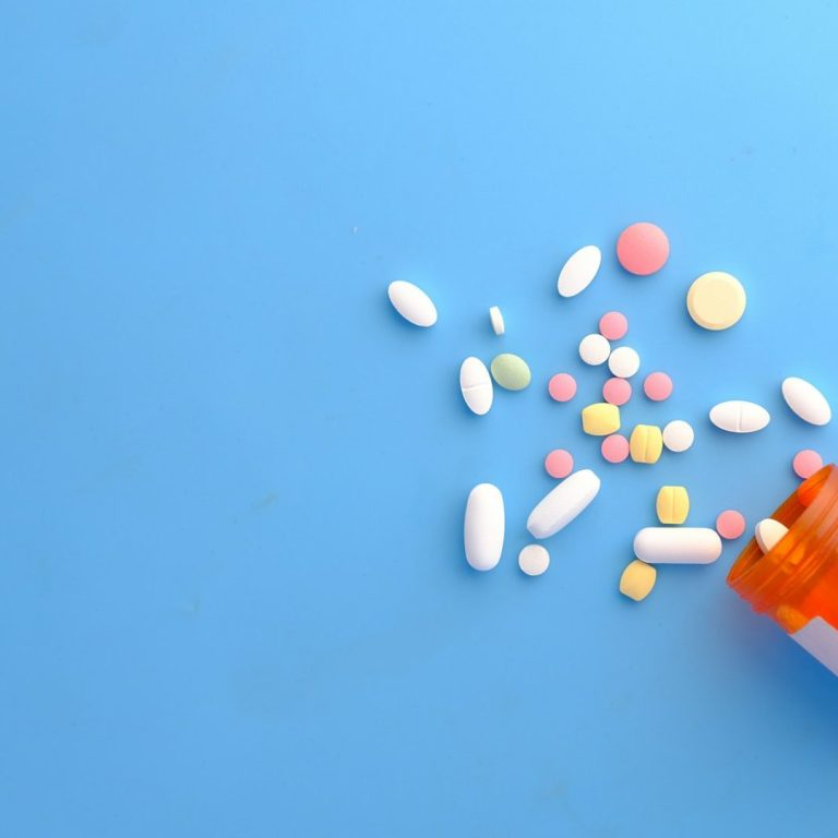 Tratamientos fisioterapia a domicilio Madrid Botiquín volcándose con pastillas y medicamentos de diversos colores sobre fondo azul.