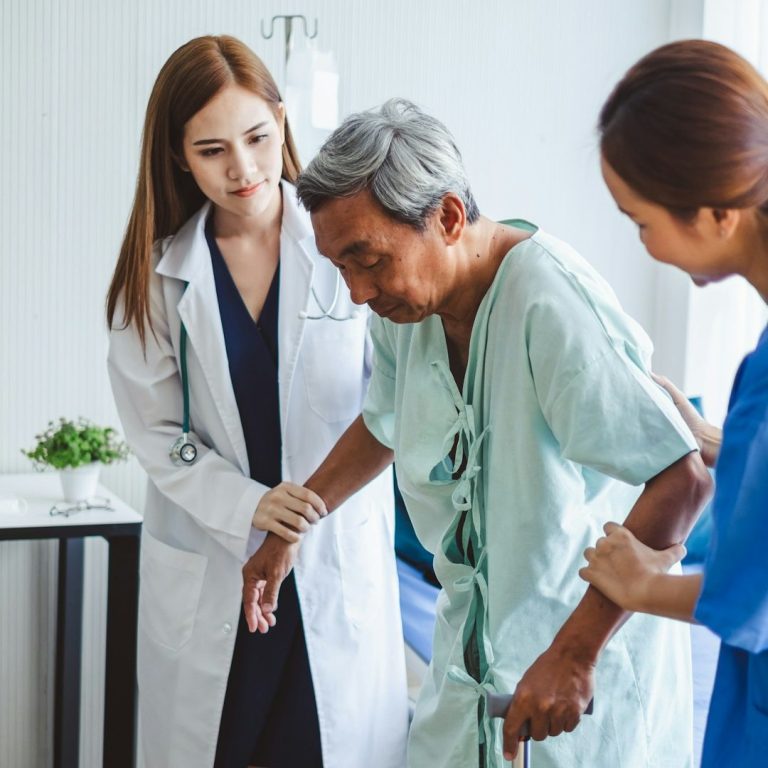 Fisioterapia a Domicilio en Moncloa y Argüelles | Colegiados Un fisioterapeuta ayudando a caminar a un paciente en un pasillo amplio o tratando a alguien en un sofá cómodo. Transmite "ayuda profesional