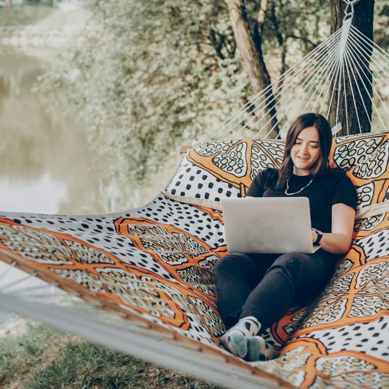 Horario Fisioterapeutas a domicilio Persona sonriente sentada en una hamaca, usando una laptop junto a un río.