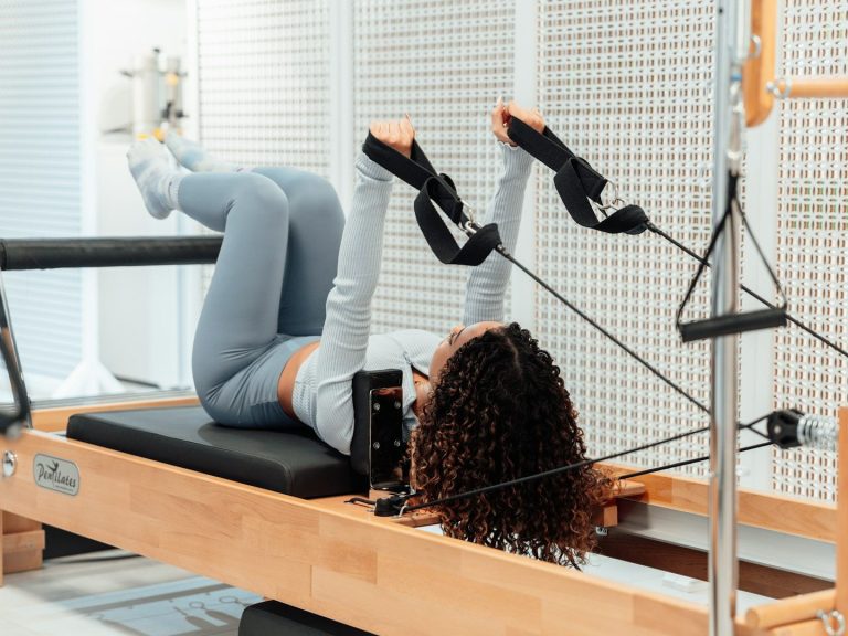 Fisioterapeutas a domicilio Mujer haciendo ejercicio en un reformador de pilates, en posición de piernas elevadas.