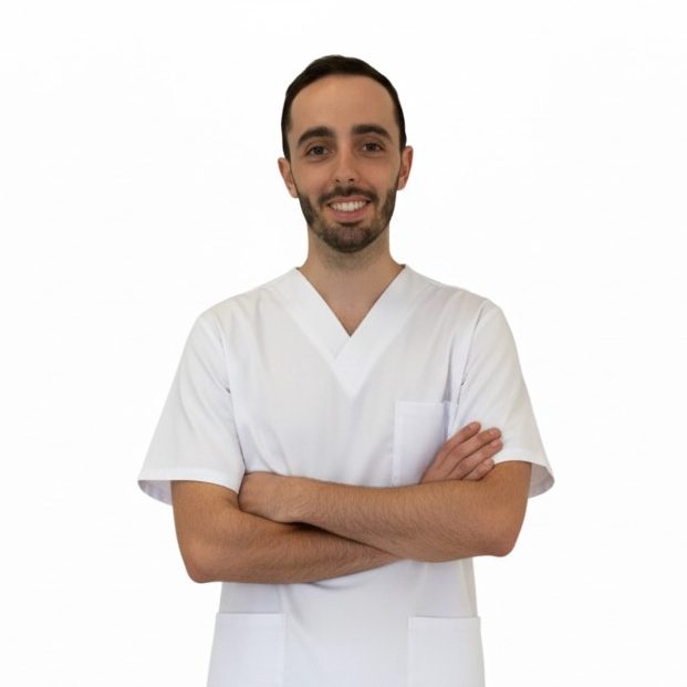 Santiago Mesas González Fisioterapeuta a domicilio Fisioterapeuta sonriente con uniforme médico, brazos cruzados, fondo blanco.