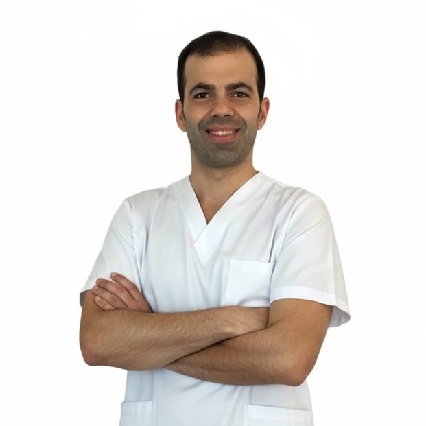 Carlos Molina Caldeiro Fisioterapeuta a domicilio Fisioterapeuta a domicilio sonriente con bata blanca, brazos cruzados y fondo blanco.