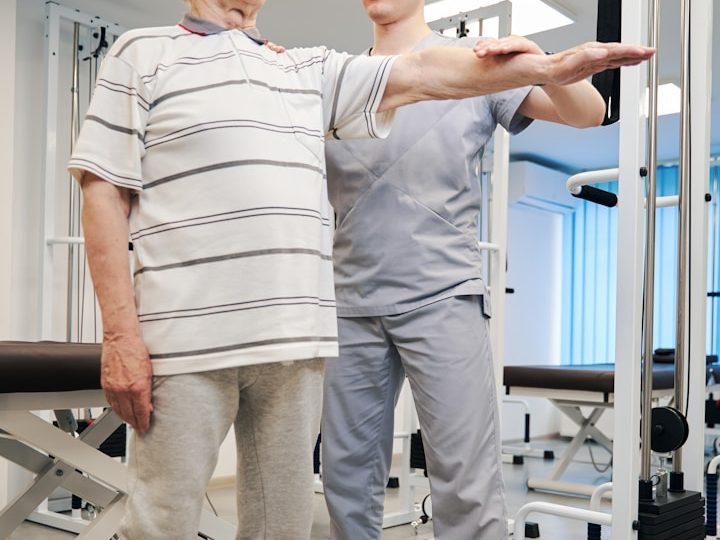 Rehabilitación a domicilio Madrid Un hombre mayor realiza ejercicios de rehabilitación con la ayuda de un fisioterapeuta.